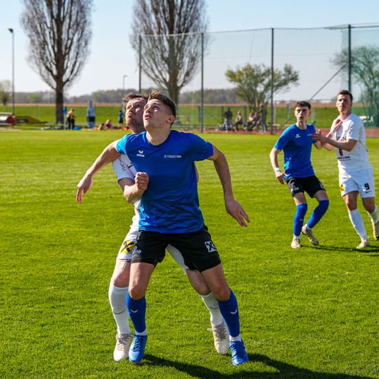 Fußballspieler rennen auf einem Feld. Ein Spieler schaut nach oben. Zwei Spieler jagen dem Ball nach. Ein Spieler mit der Nummer 9 auf seinem Trikot läuft.