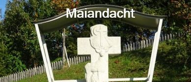 Ein weißer Kreuz mit Schnitzereien steht auf einem Rasen. Eine kleine Statue eines Soldaten steht davor. Das Kreuz ist von einer weißen Struktur umschlossen.