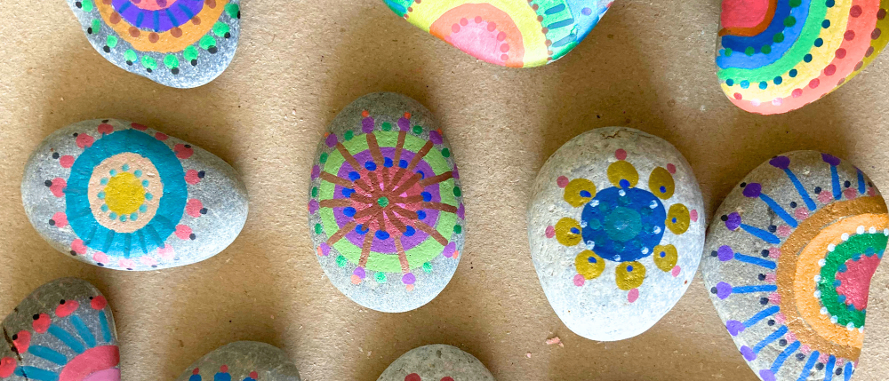 Eine Sammlung bemalter Steine mit verschiedenen bunten Mustern. Jeder Stein hat ein einzigartiges Muster aus Kreisen und Linien, einschließlich Lila, Gelb, Grün und Blau.