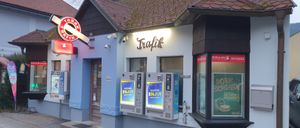 A store front with a brown roof and blue walls. There is a sign that reads 'Trafik'. Two machines are attached to the wall. The sign above the machines reads 'Enjoy'.