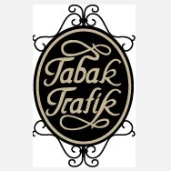 Das Bild zeigt ein Logo für 'Tabak Trafik' mit einem schwarzen ovalen Rahmen und komplizierten schwarzen und goldenen Designs. Der Text ist stilisiert und zentral im Oval platziert.