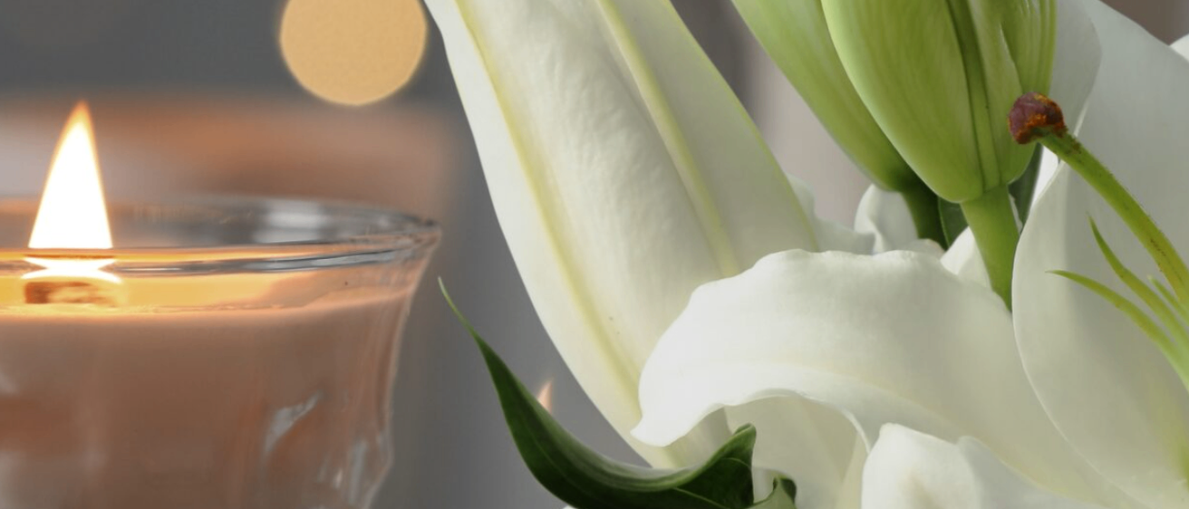 Nahaufnahme einer weißen Lilienblüte mit einem unscharfen Kerzenhintergrund. Die Blume hat eine glänzende Oberfläche.