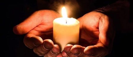 Zwei Hände halten sanft eine brennende Kerze, deren Flamme die Umgebung in einer dunklen Umgebung erhellt.