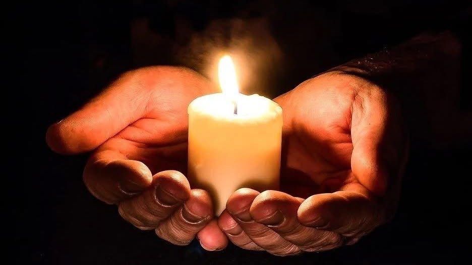 Zwei Hände halten eine brennende Kerze in der Dunkelheit, die Umgebung mit ihrem warmen Licht erhellend.