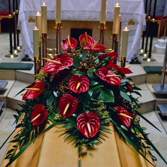 Ein mit roten Blumen bedeckter Sarg steht vorn in einer Kirche mit brennenden Kerzen vor dem Altar.