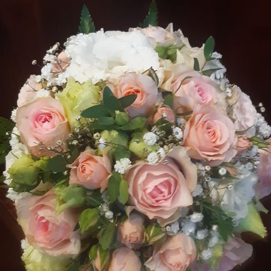 Ein Nahaufnahme eines Straußes mit verschiedenen rosa und weißen Blumen, einschließlich Rosen, Babys Atem und Nelken, auf einem dunklen Hintergrund angeordnet.