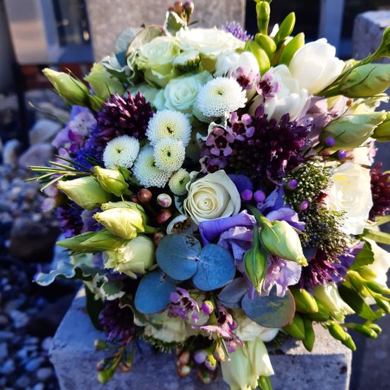 Eine große Blumenarrangement mit einer Mischung aus weißen, lila und blauen Blumen auf einem Betonblock.
