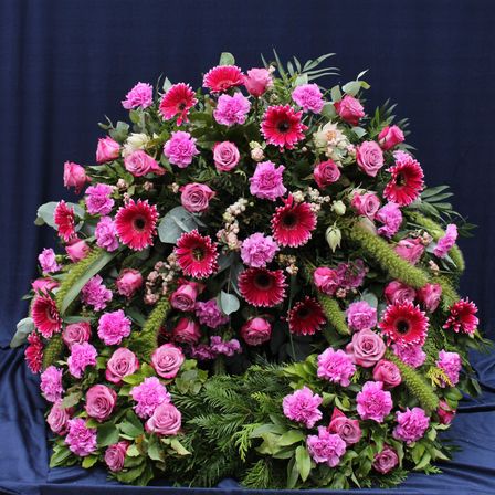 Eine kreisförmige Blumenarrangement mit einer lebhaften Mischung aus rosa Rosen, roten Gerbera und grünen Blättern auf blauem Hintergrund.