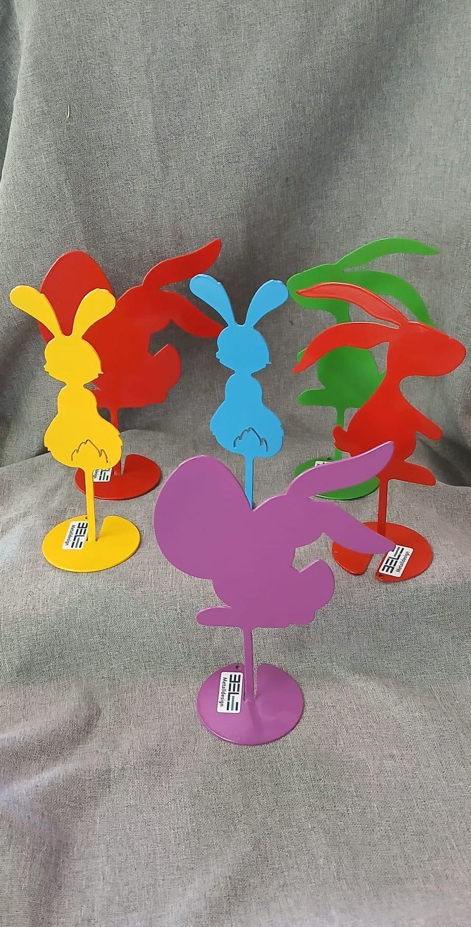 A collection of six colorful metal rabbit sculptures on a gray background. Each rabbit is painted in a different color and stands on a matching base.