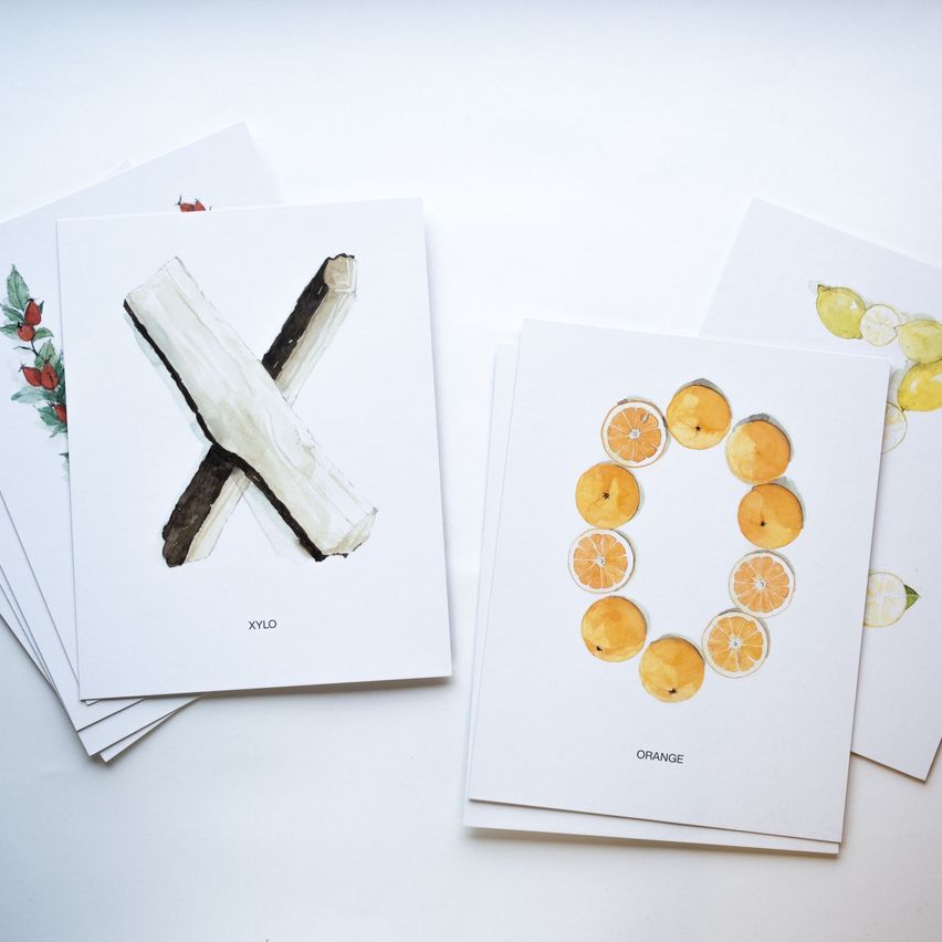 A stack of cards with 'XYLO' written in black and a cross-like figure made of wood. Next to it, a card with the word 'ORANGE' and a design of orange slices forming a circle.