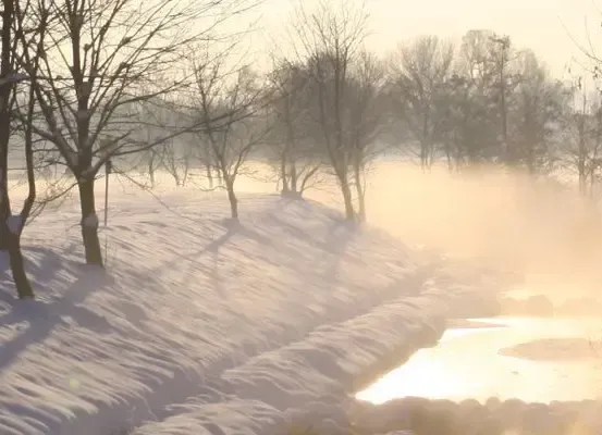 Eine verschneite Landschaft mit einem Fluss, der durch sie fließt, umgeben von laublosen Bäumen. Nebel steigt aus dem Fluss auf, und der Himmel ist klar und hell.