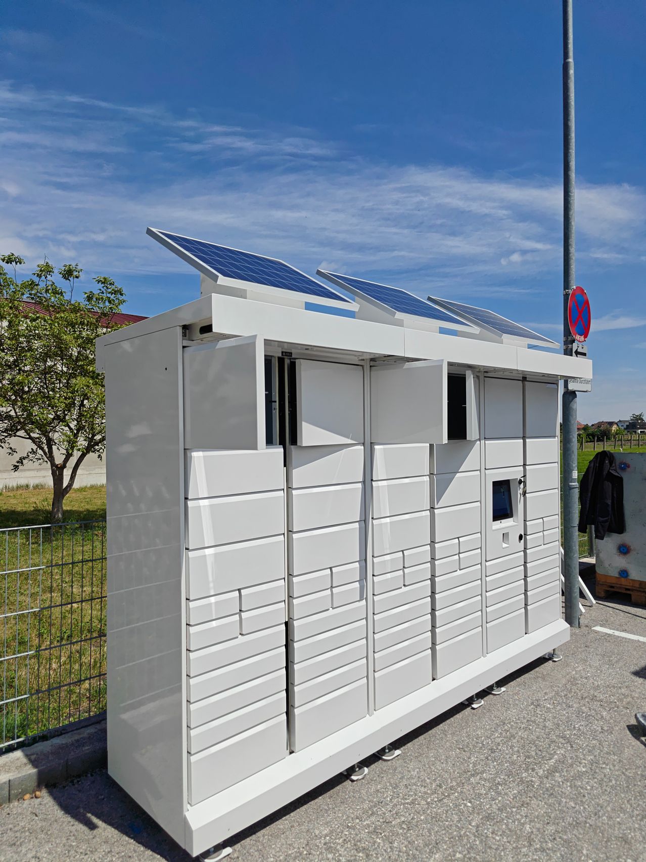 Ein weißer solarbetriebener Container mit Solarmodulen auf dem Dach steht im Freien in der Nähe eines Zauns und einer Rasenfläche mit einem Baum.