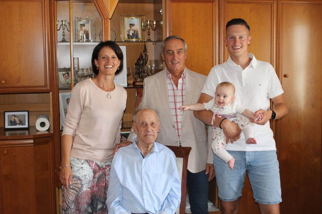 Eine vierköpfige Familie posiert für ein Foto in einem Raum mit Holzschränken und Regalen. Das Baby wird von einem Mann gehalten.
