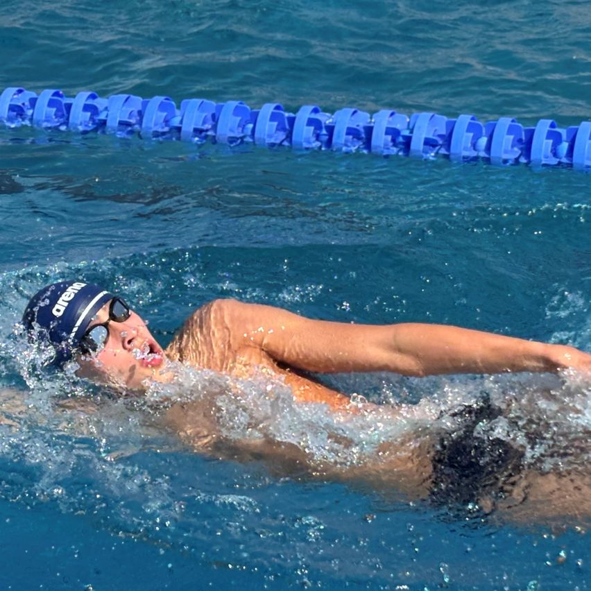 Ein Schwimmer mit blauer Kappe und Schwimmbrille schwimmt in einem Becken mit blauen Bahnmarkierungen.