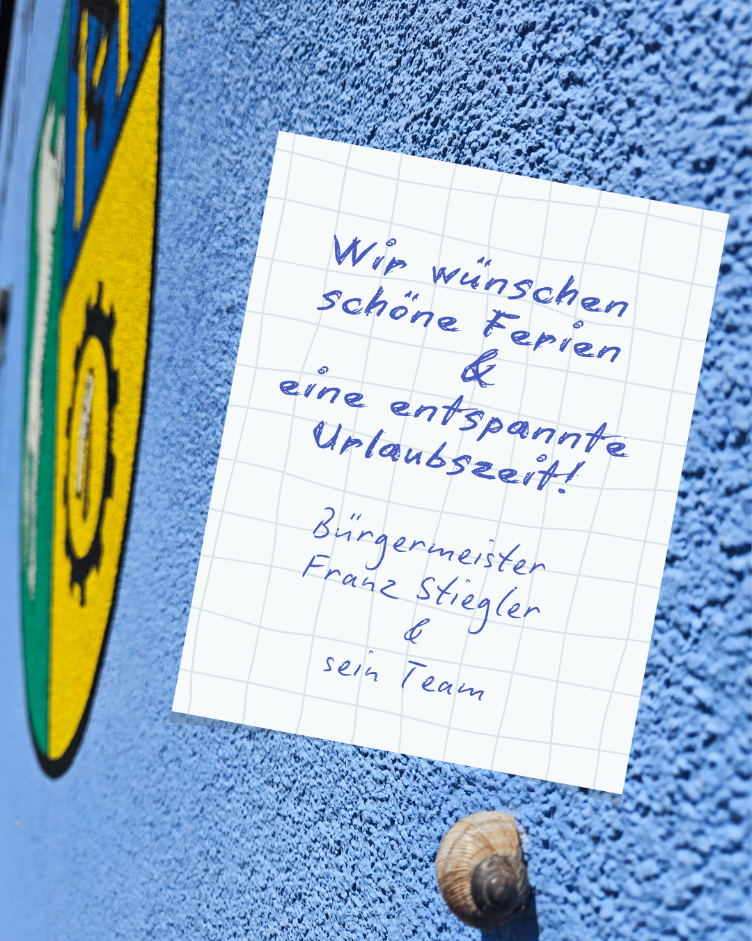 Eine handgeschriebene Notiz auf einer blauen Wand mit einem Gittermuster. Es steht 'Wir wünschen schöne Ferien & eine entspannte Urlaubszeit!' von Bürgermeister Franz Stiegler und seinem Team.