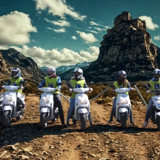 Eine Gruppe von Menschen in Helmen und grünen Westen fährt mit Rollern auf einem Schotterweg, mit Bergen im Hintergrund.