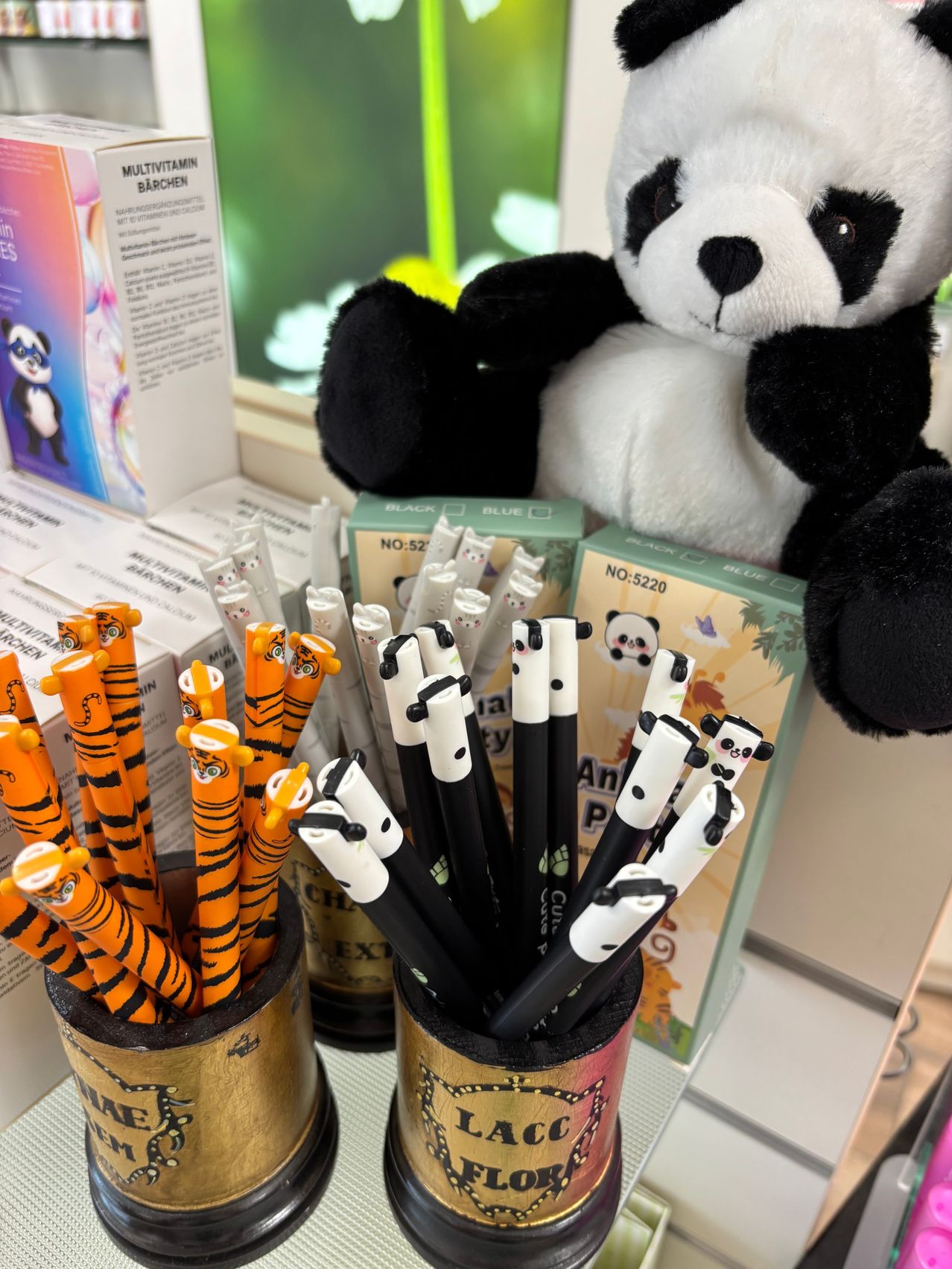 Two containers filled with colorful animal-themed pens, including ones shaped like tigers and pandas, with a panda plush in the background.