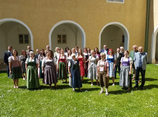 Eine Gruppe von Menschen in traditioneller bayerischer Kleidung posiert für ein Foto vor einem Gebäude mit Bogenfenstern und -türen.