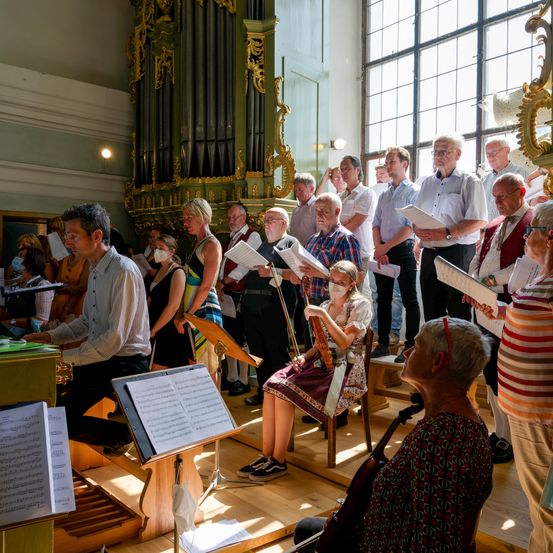 Ein Chor aus Erwachsenen in Freizeitkleidung singt in einer Kirche mit einer Orgel im Hintergrund.