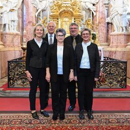 Fünf Personen stehen vor einem kunstvollen Altar in einer Kirche und posieren für ein Foto. Dahinter sind Statuen und Kerzen zu sehen.