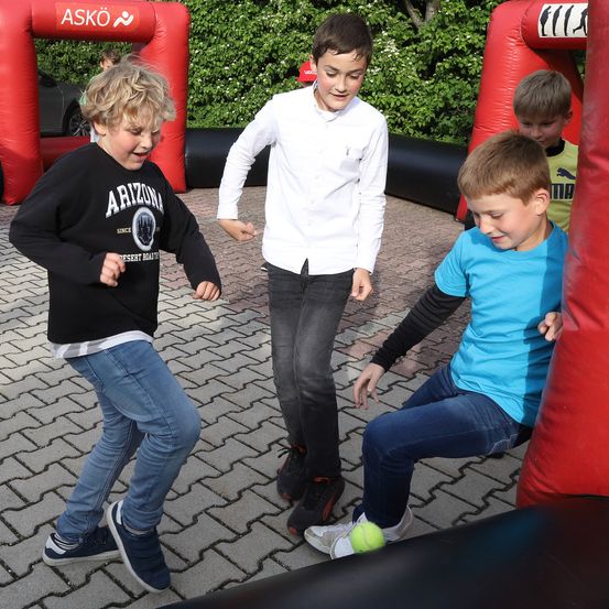 Vier Jungen spielen in einem aufblasbaren Hindernisparcours. Ein Junge trägt ein weißes Hemd und schwarze Hose, ein anderer ein schwarzes Sweatshirt mit dem Wort Arizona.