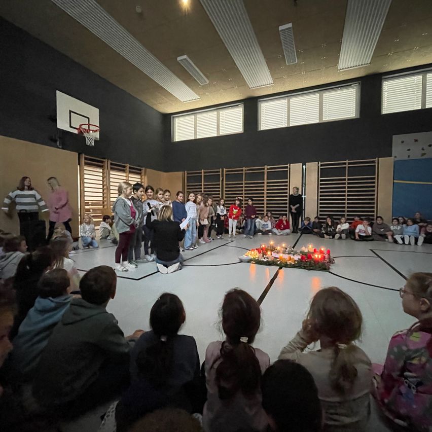 Eine Gruppe von Kindern und Erwachsenen versammelt sich in einer Turnhalle, einige knien im Gebet um eine Kerzen-Installation.