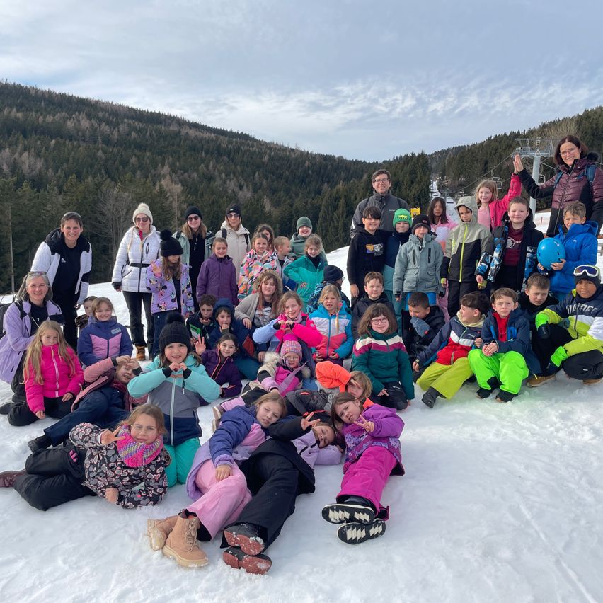 Eine Gruppe von Kindern und Erwachsenen posiert für ein Foto im Schnee mit Bergen im Hintergrund.