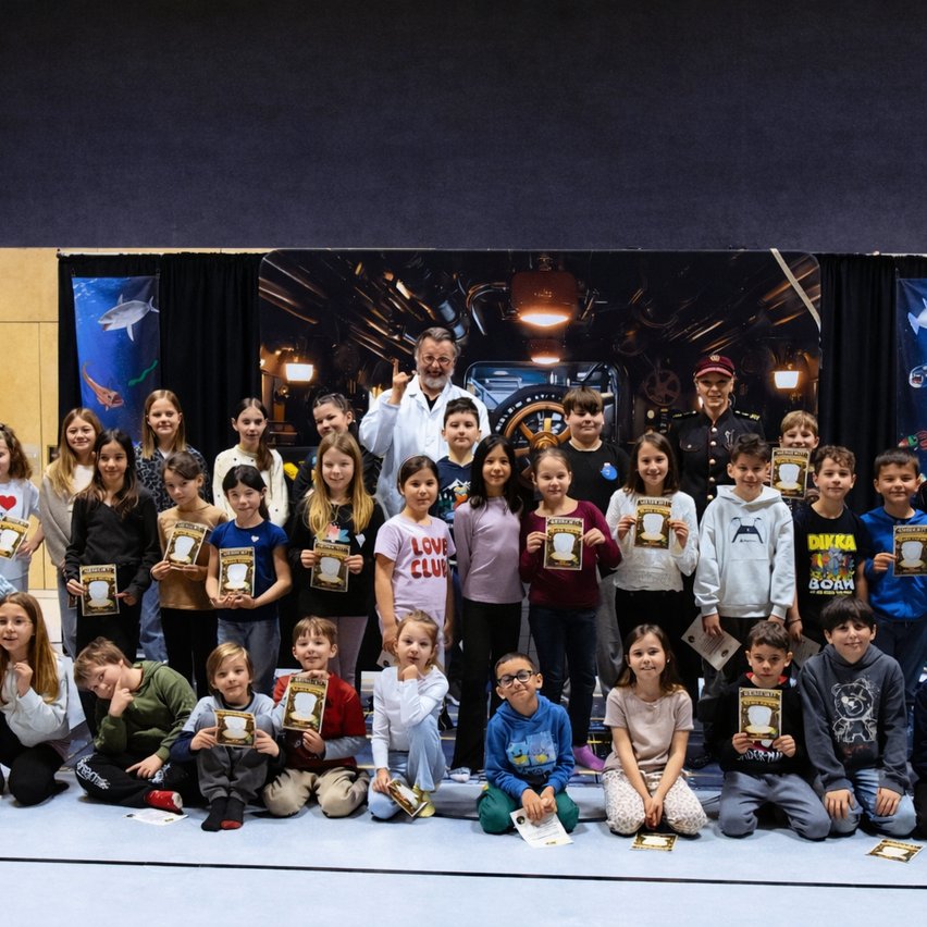 Eine Gruppe von Kindern in verschiedenen Kleidungsstücken und Posen, die Urkunden halten, posiert für ein Foto in einer Schule. Eine Frau und ein Mann stehen in der Mitte.