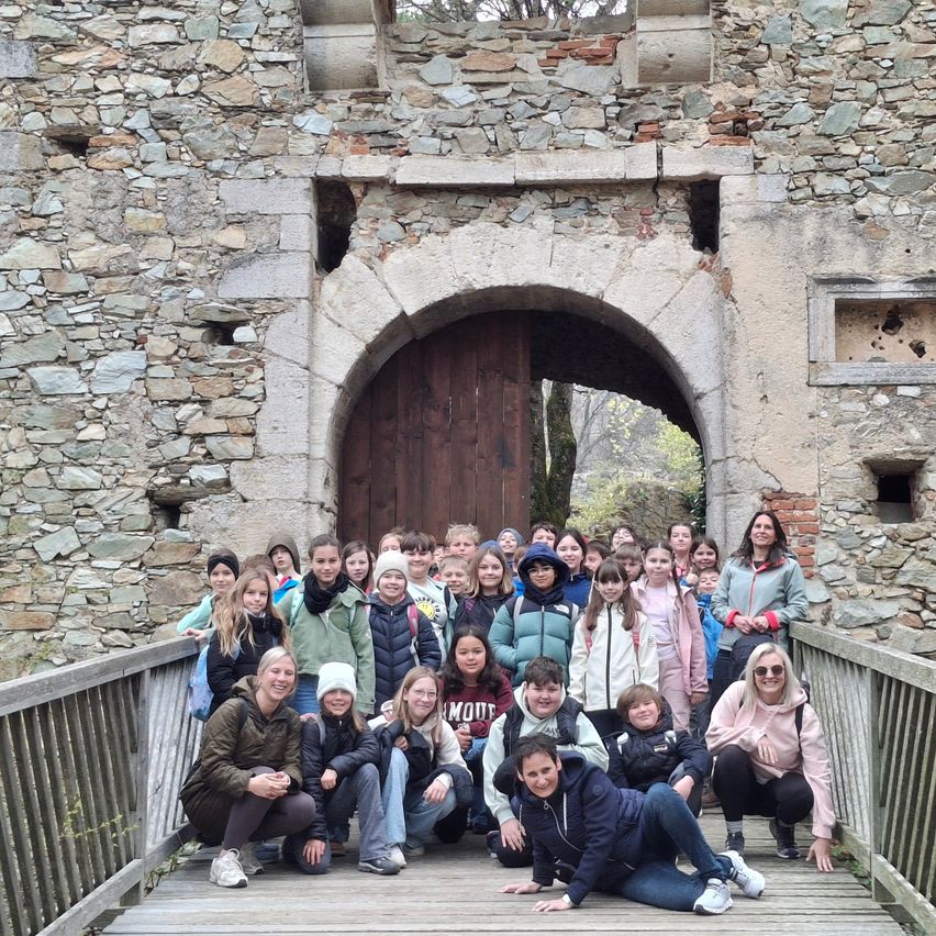 Eine Gruppe von Kindern und zwei Erwachsenen posiert vor einem alten Steingebäude mit einem gewölbten Eingang.