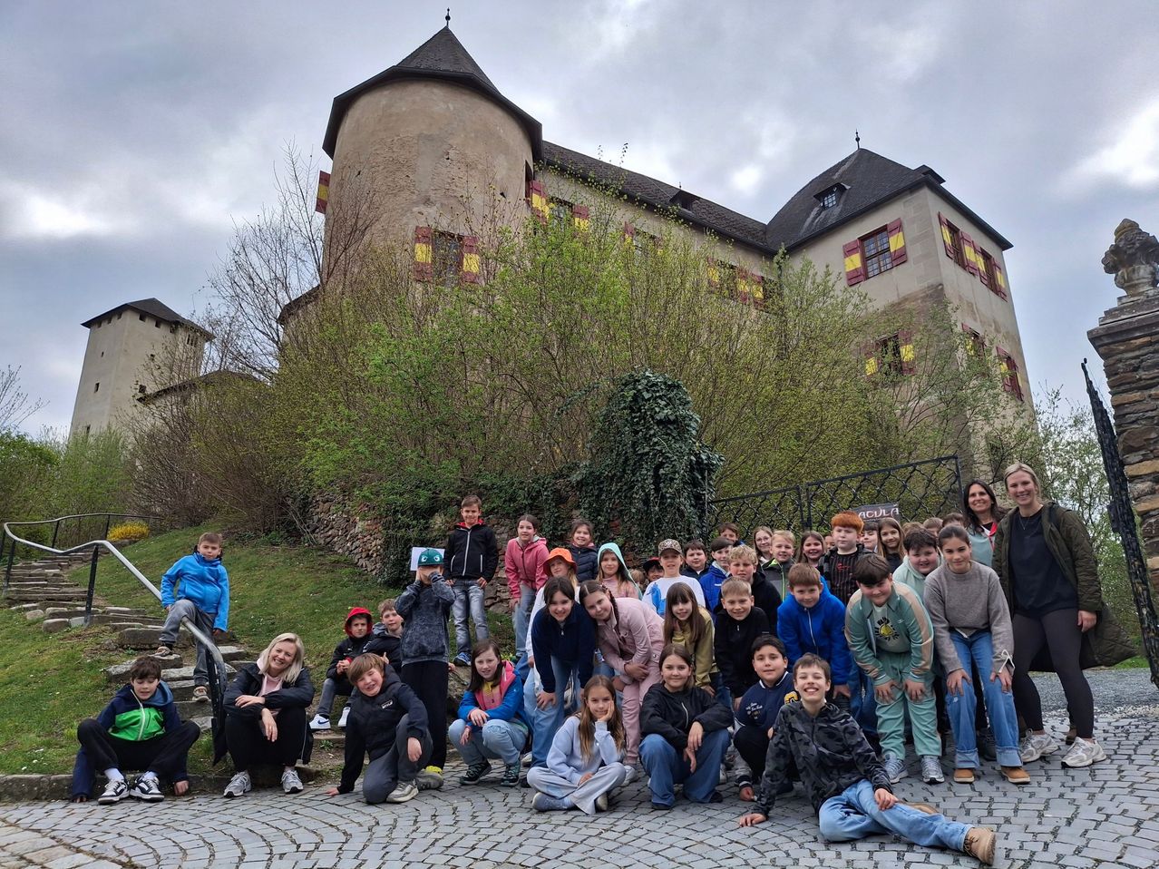Eine Gruppe von Kindern und Erwachsenen posiert für ein Foto vor einem alten Schloss mit gelb gestreiften Fenstern.