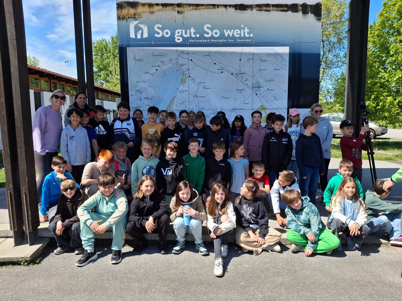 Eine Gruppe von Kindern und Erwachsenen posiert für ein Foto vor einer großen Karte mit einer landschaftlichen Kulisse.