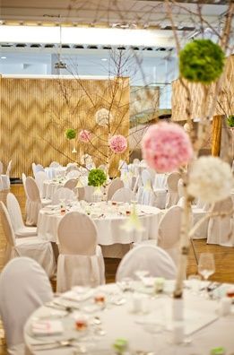 Ein Bankettsaal ist mit pinken und grünen Blumenarrangements auf Tischen und Stühlen dekoriert, mit einem Hintergrund aus Holzwänden und einer Treppe.