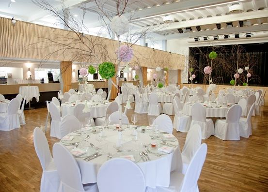 Ein Indoor-Veranstaltungsort mit weißen Stühlen und Tischen, Holzböden und dekorativen Elementen.