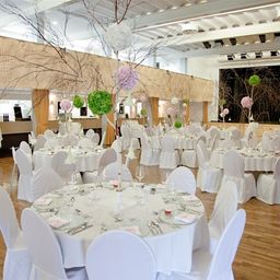 Ein Indoor-Veranstaltungsort mit weißen Stühlen und Tischen, Holzböden und dekorativen Elementen.