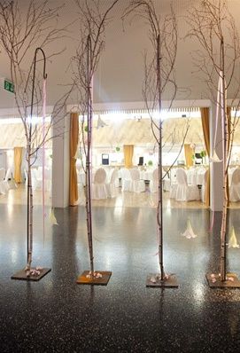 Ein Raum mit schwarzem Boden, Zweigen in der Mitte und weißen Stühlen, die für ein Essensarrangement aufgestellt sind.