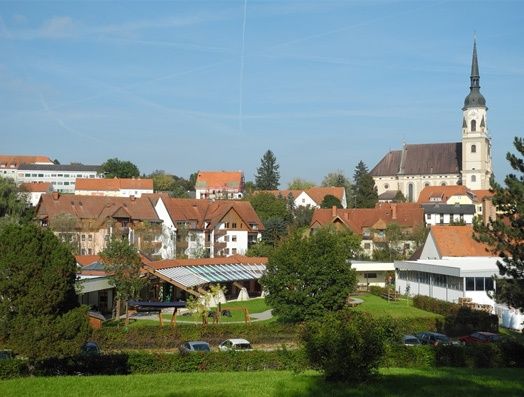 Eine Stadt mit einer Kirche im Zentrum, umgeben von Gebäuden und Bäumen, unter einem klaren blauen Himmel.