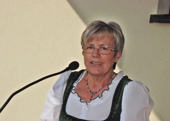 Eine Frau mit Brille und einem weißen und grünen Oberteil steht vor einem Mikrofon.