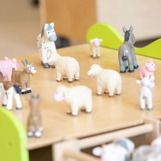 Eine Sammlung von Farmtierspielzeug in verschiedenen Farben und Größen steht auf einem Holztisch.