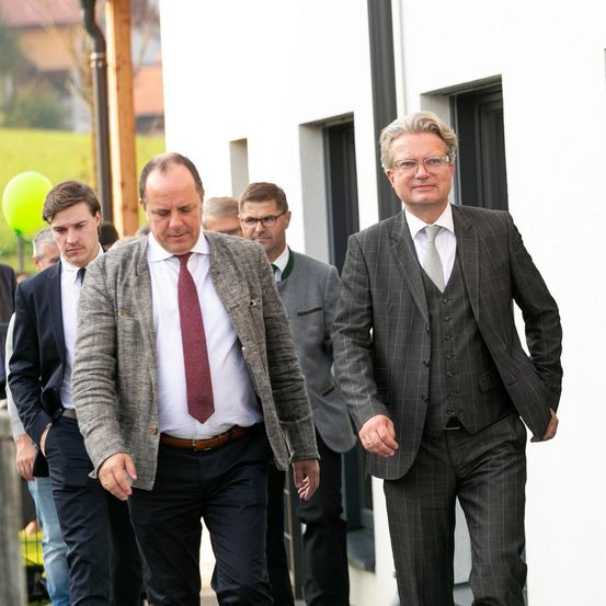 Mehrere Männer in Anzügen und Krawatten gehen einen Weg entlang. Ein gelber Luftballon ist im Hintergrund zu sehen.