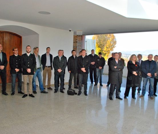 Eine Gruppe von Menschen steht in einem Raum mit großen Fenstern und einer Holztür. Sie sind in Winterkleidung gekleidet.