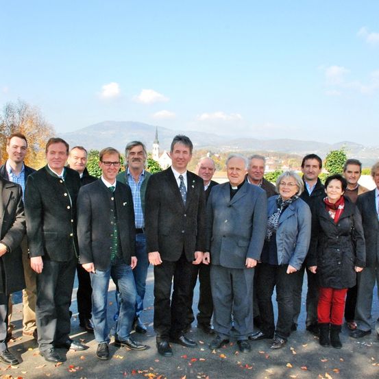 Eine Gruppe von Menschen in formeller Kleidung posiert für ein Foto an einem sonnigen Tag, mit einer malerischen Bergkette im Hintergrund.