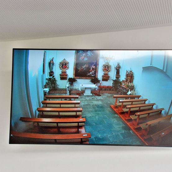 Eine digitale Aufnahme des Kircheninneren mit Reihen von Kirchenbänken, einem zentralen Altar und religiösen Statuen, alles unter einer kuppelartigen Decke.