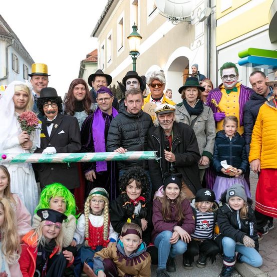 Eine Gruppe von Menschen, in verschiedenen Kostümen gekleidet, posiert für ein Foto auf einer Straße mit Gebäuden und Laternen im Hintergrund.