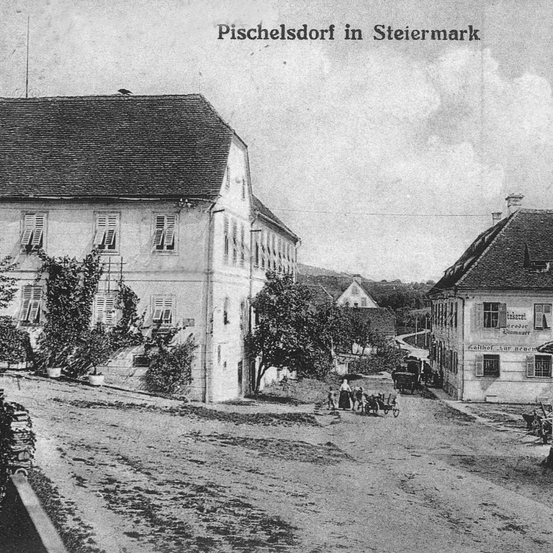Ein altes Schwarz-Weiß-Foto zeigt eine Straße in Pischelsdorf, Steiermark, mit Gebäuden, Menschen und Kutschen.