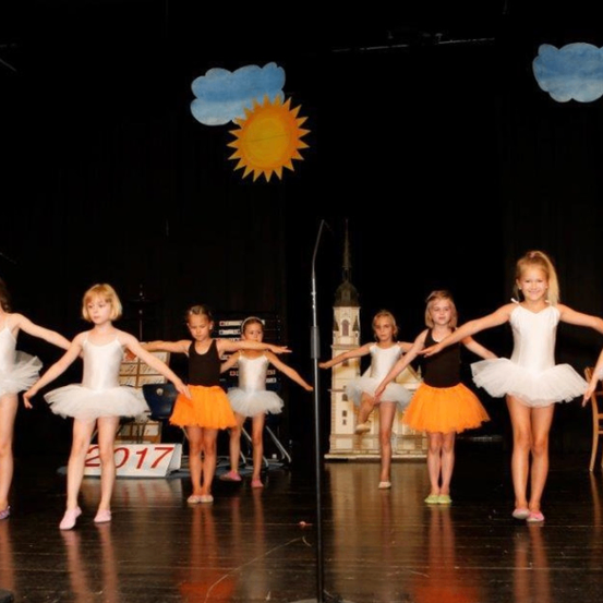 Kleine Mädchen in weißen Tutus führen einen Ballettaufführung auf einer Bühne mit einem Hintergrund von Sonne und Wolken auf. Das Jahr 2017 ist auf dem Hintergrund sichtbar.
