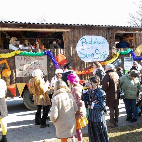 Eine Gruppe von Menschen steht vor einem für eine Veranstaltung geschmückten Lastwagen. Mehrere Personen sitzen im Lastwagen, eine Person hält ein Mikrofon. Der Lastwagen trägt ein Schild mit der Aufschrift 'Mit Hel Bohlen den Popdibar eine Karaoke Show mit Liv'.
