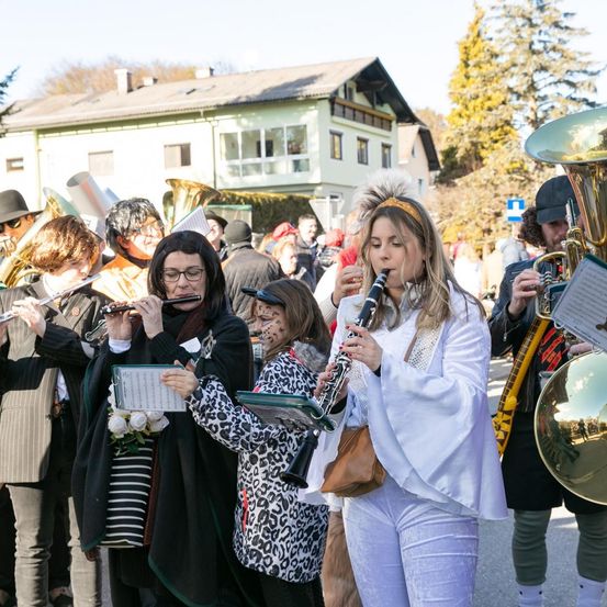 Ein Marschkapelle spielt vor einem Haus. Eine Frau spielt Klarinette, während andere Flöte und Tuba spielen. Sie sind in Kostümen gekleidet.