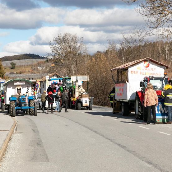 Eine Gruppe geschmückter Traktoren für eine Parade steht am Straßenrand, mit Menschen, die herumlaufen.