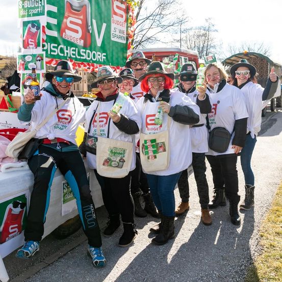 Eine Gruppe von Menschen in weißen Hemden und Hüten mit roten Haaren und Brillen posiert für ein Foto mit Flaschen und Taschen an einem sonnigen Tag.