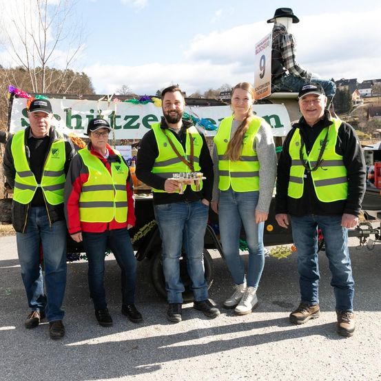 Fünf Personen in neongrünen Warnwesten stehen vor einem Fahrzeug mit dem Schriftzug 'hitze'. Eine Person sitzt auf dem Fahrzeug.